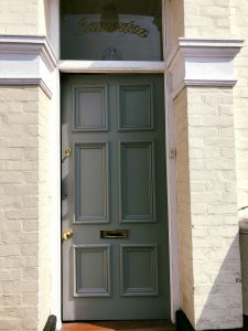 a soft sage green painted front door with brass hardwear